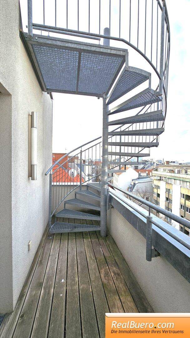 Kleiner Balkon mit Holzbelag und einer Wendeltreppe, die zur Dachterrasse führt.