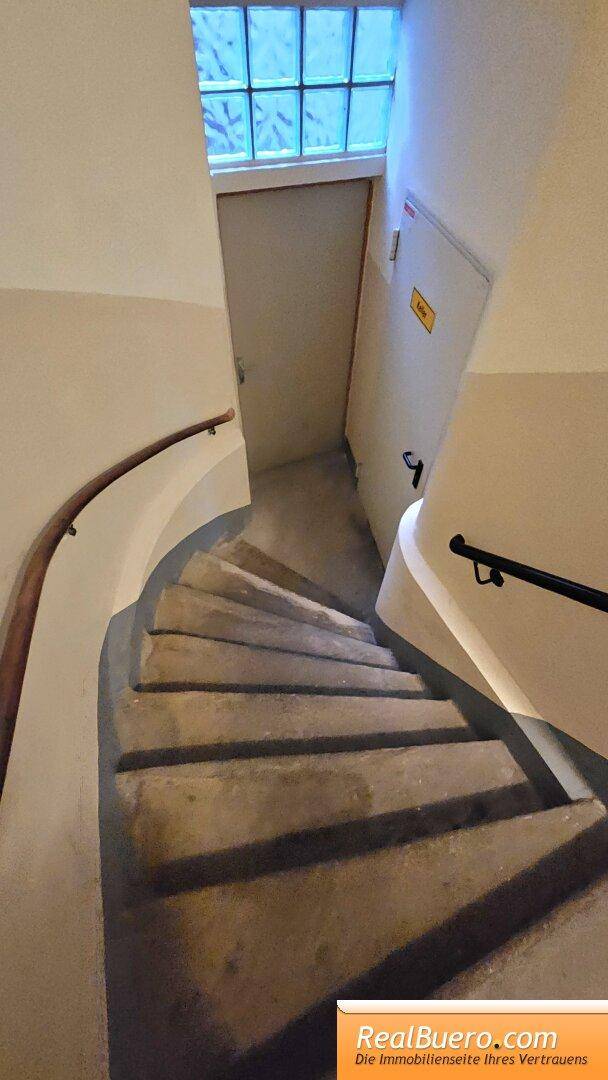 Wendeltreppe in einem älteren Gebäude mit einem Fenster am oberen Ende, das natürliches Licht hereinlässt. Die Treppe ist gut erhalten.