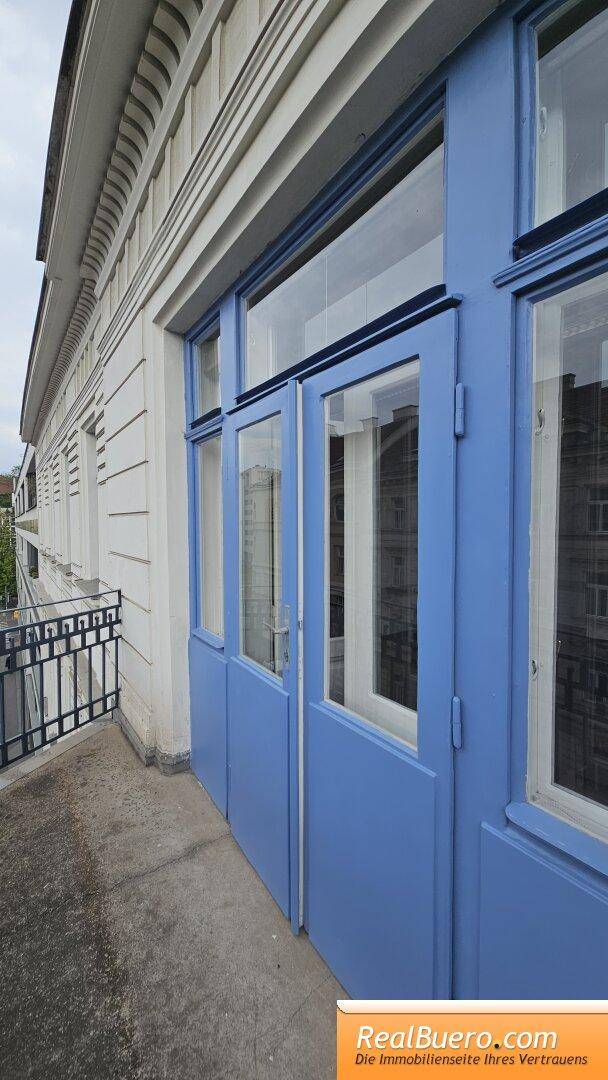 Blauer Balkonzugang mit großen Fenstern und Blick auf die historische Fassade des Gebäudes.