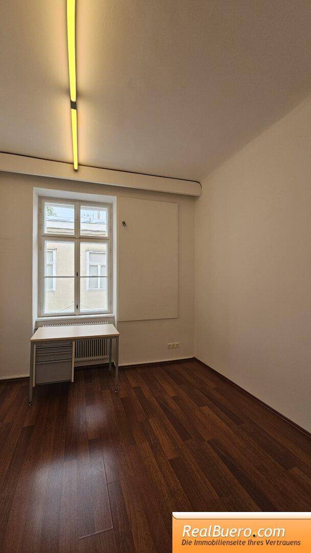 Kleiner Büroraum mit Holzfußboden, einem Fenster und einem einfachen Schreibtisch.