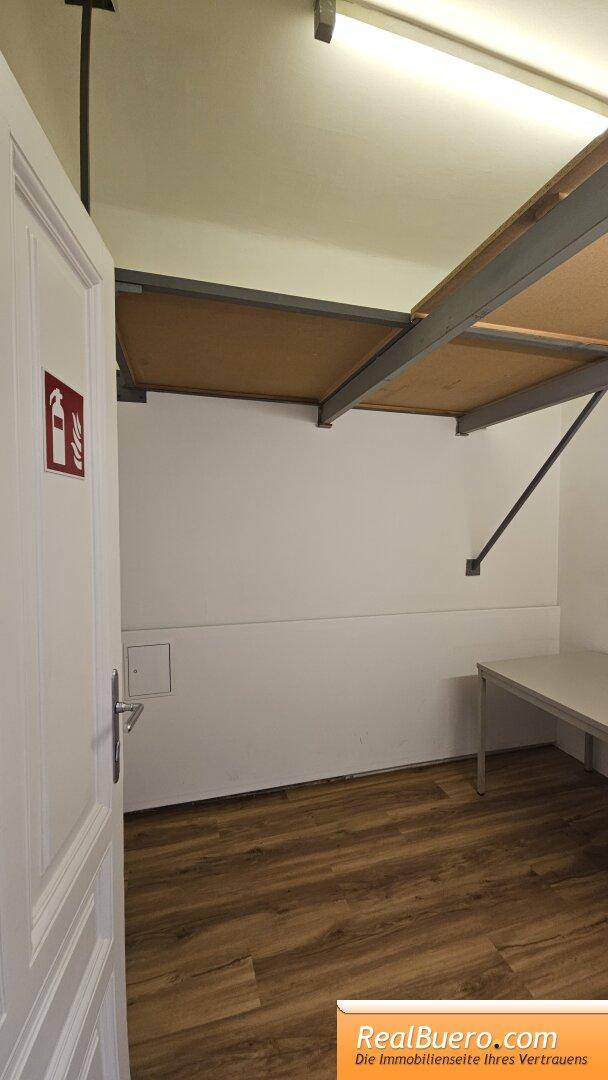 Raum mit Holzboden, einer Ablage unter der Decke und einer Tür mit Brandschutzzeichen.
