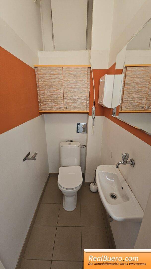 Schmale Toilette mit WC, Waschbecken und orange-weißen Wänden.