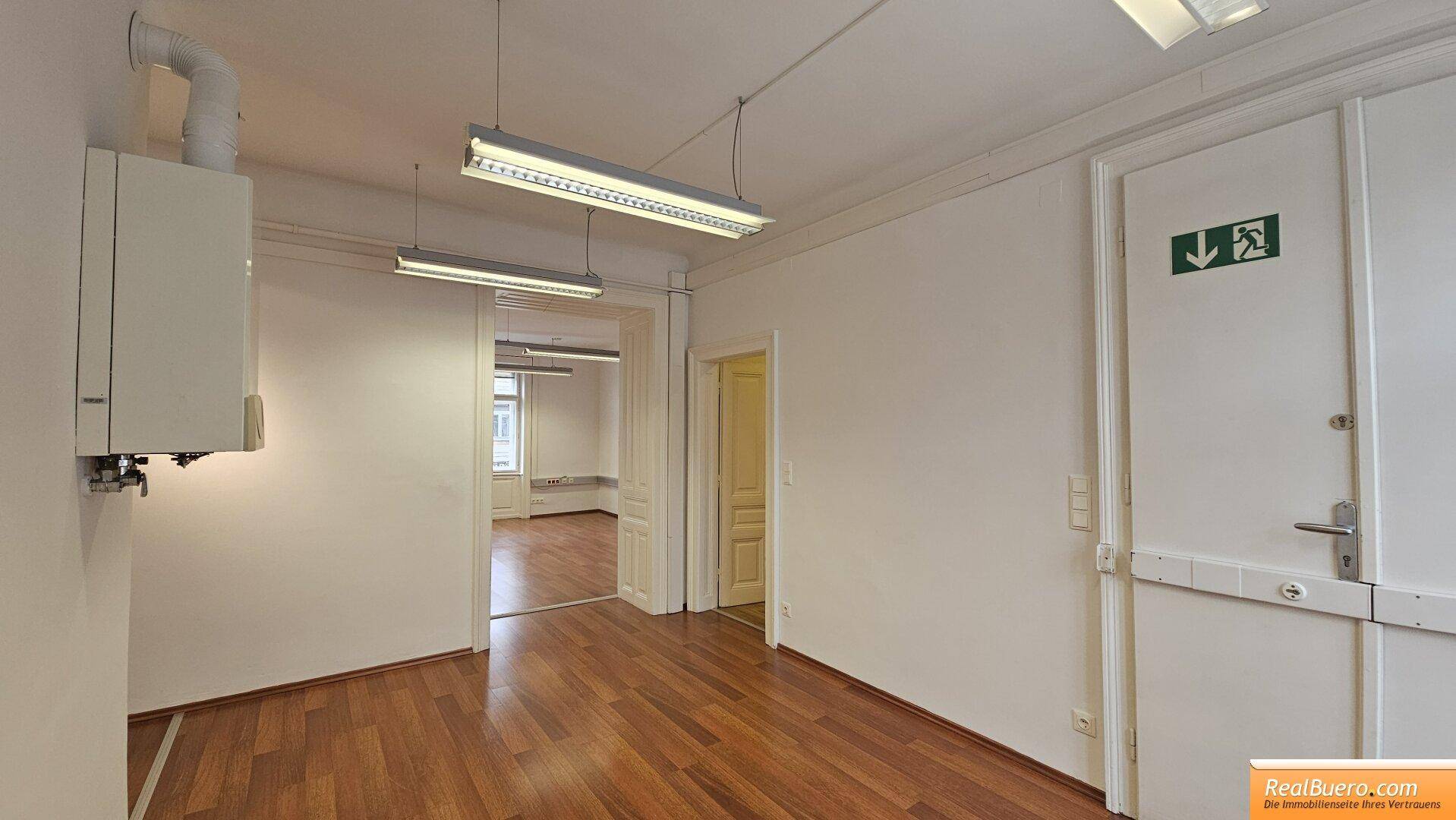 Büroraum mit Holzfußboden, Notausgangstür und Blick in angrenzende Räume.