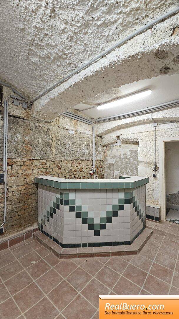 Detailansicht einer gefliesten Theke mit geometrischem Muster in einem Kellerraum, umgeben von rauen Wänden.
