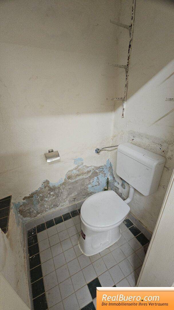 Einfaches WC mit Fliesenboden und unverputzten Wänden, das eine grundlegende Ausstattung bietet.