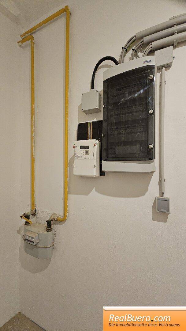 Nahaufnahme eines Gaszählers und eines elektrischen Verteilerkastens mit sichtbaren Leitungen.