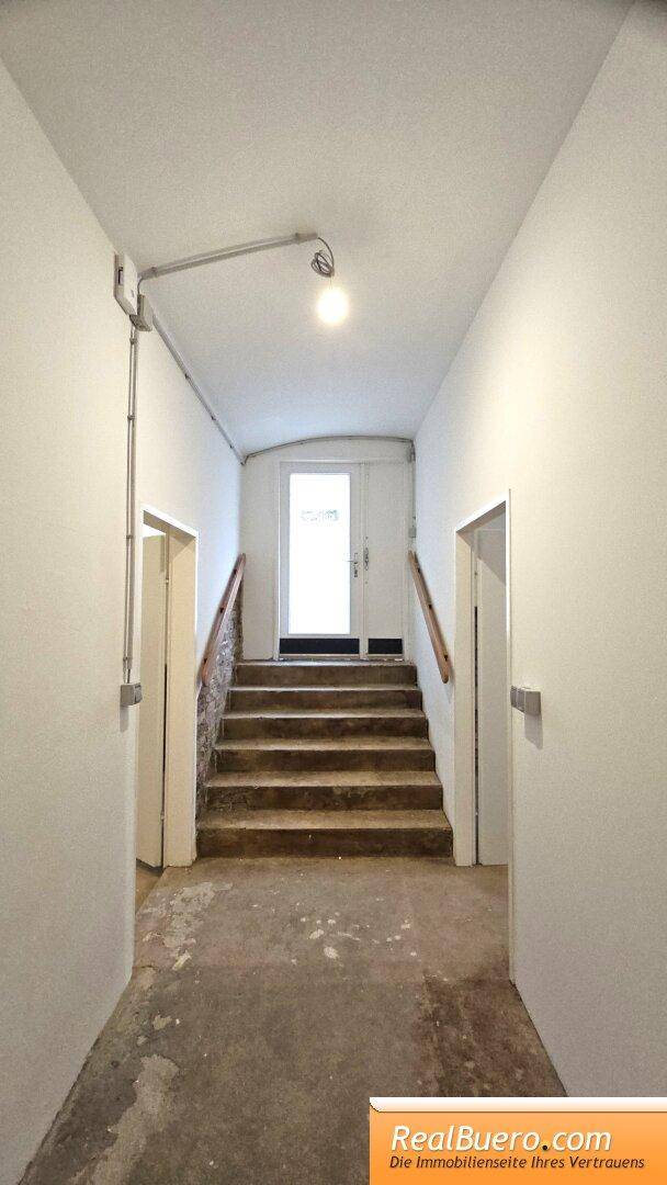 Langer Flur mit einer Treppe, die zu einer Doppeltür führt, und einfachen Wänden.