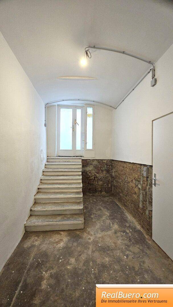 Heller Flur mit einer Treppe, die zu einer Doppeltür führt, und unverputzten Ziegelwänden.