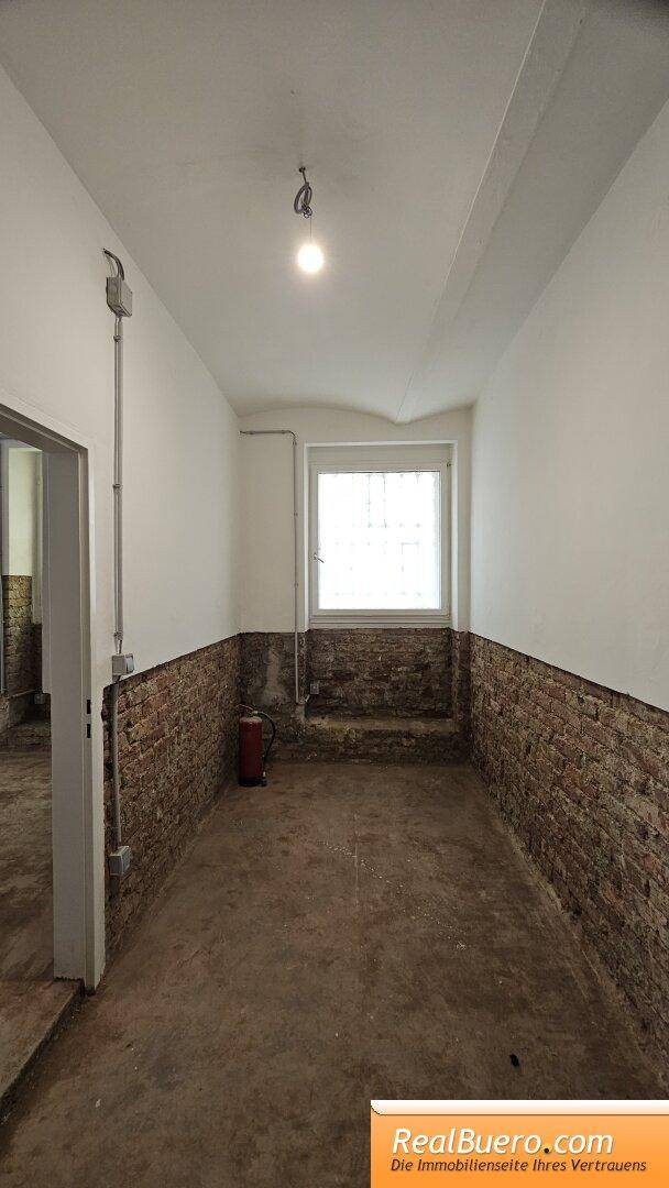 Langer, schmaler Flur mit einem Fenster, freigelegten Ziegelwänden und einem Feuerlöscher.
