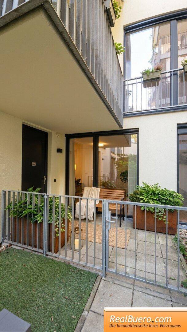 Gemütliche, eingezäunte Terrasse im Erdgeschoss mit Sitzgelegenheiten und grünen Pflanzen in Kübeln.