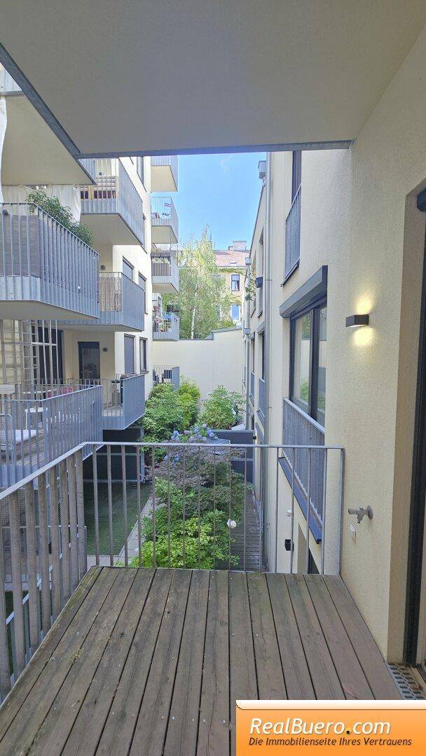 Heller Balkon mit Holzbelag und Metallgeländer, bietet einen ruhigen Blick auf den grünen Innenhof.