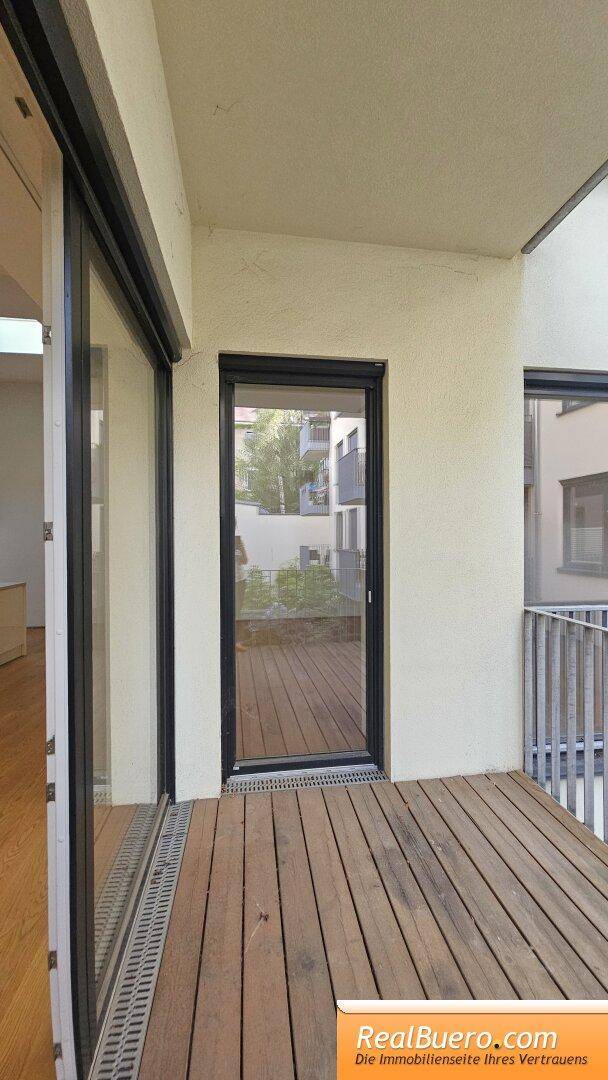 Heller Balkon mit Holzboden und großen Glasfronten, die viel Tageslicht hereinlassen.