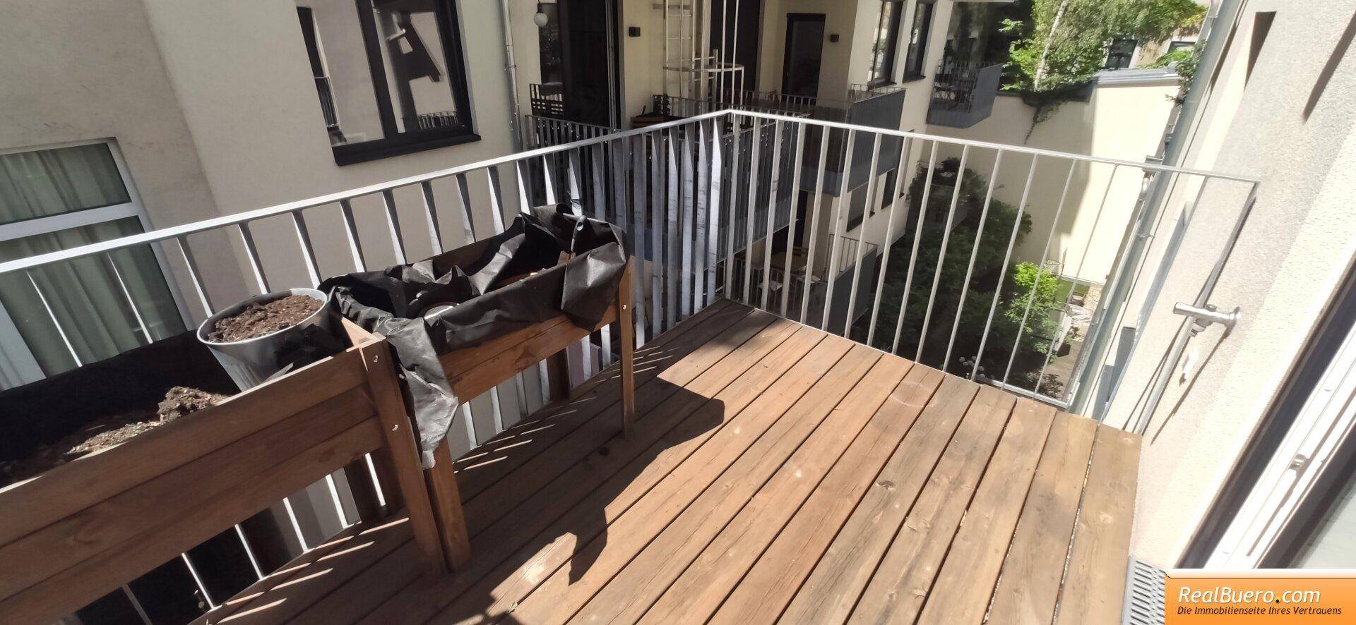 Balkon mit Holzdielenboden und Metallgeländer, bereit für individuelle Bepflanzung und Nutzung.