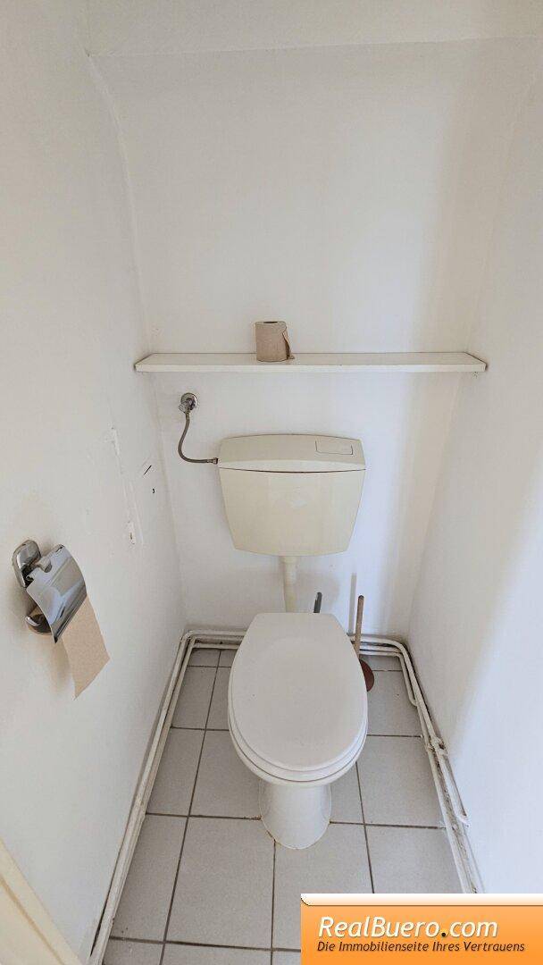 Kleines Gäste-WC mit Toilette, Regal und Fliesenboden, einfach und funktional gestaltet.
