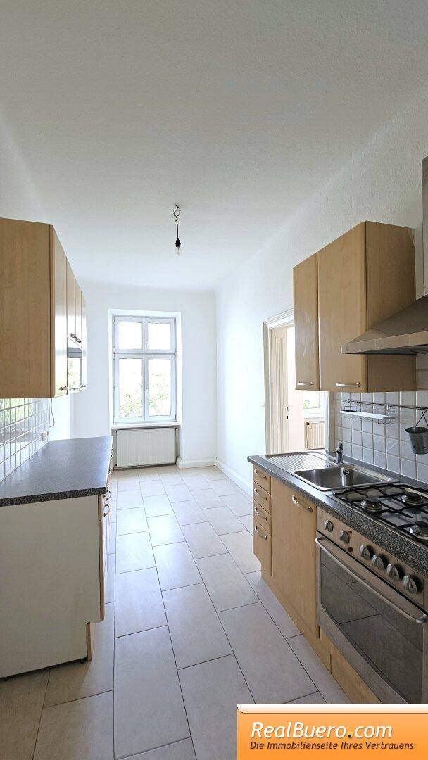 Helle Küche mit Holzfronten, Fliesenboden und einem Fenster, das viel Tageslicht hereinlässt.