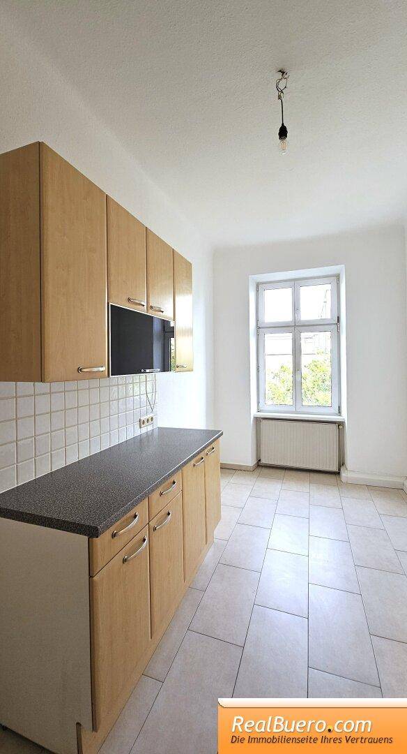 Küchenzeile mit hellen Holzschränken, dunkler Arbeitsplatte und einem Fenster, das den Raum erhellt.