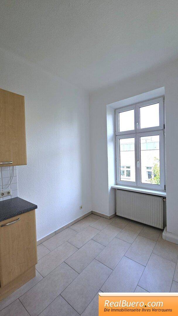 Heller Küchenbereich mit Fliesenboden und einem großen Fenster, das den Raum mit Tageslicht füllt.
