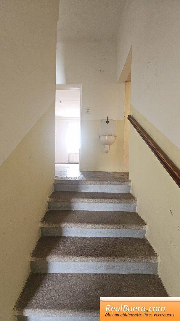 Treppenhaus mit Steinstufen und Holzgeländer, führt zu einem weiteren Flur mit Waschbecken.