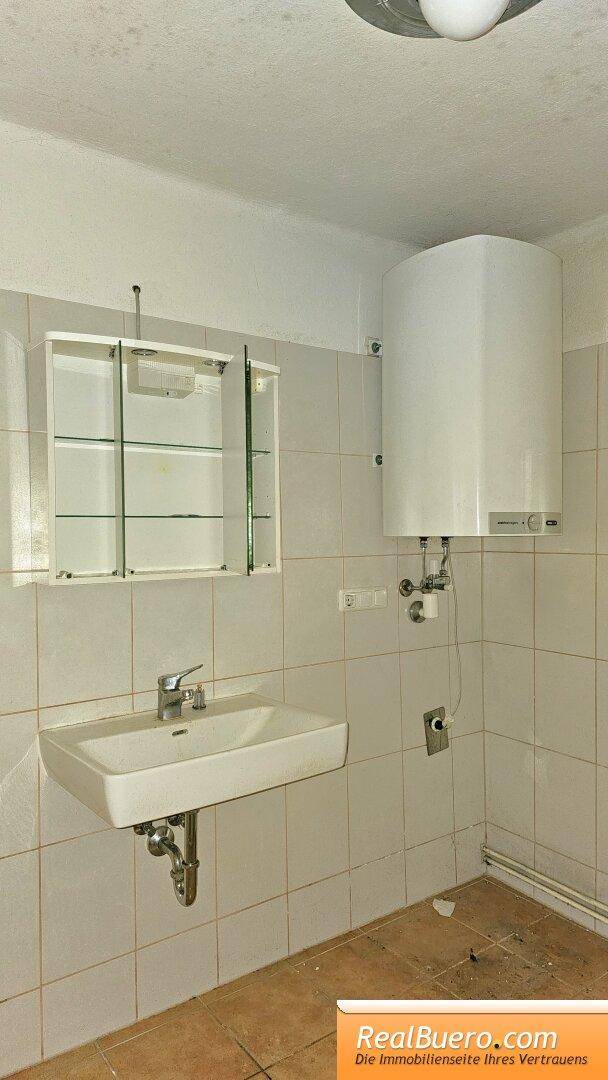 Badezimmer mit Waschbecken, Spiegelschrank und Boiler, gefliest in hellem Beige.