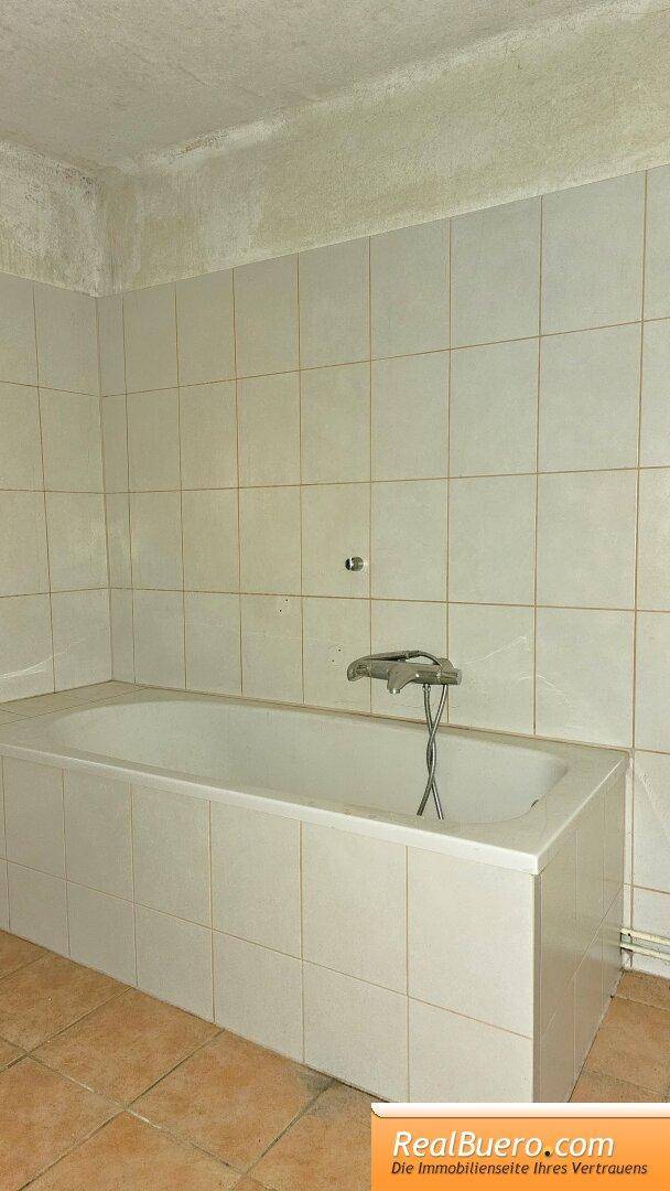 Badezimmer mit eingebauter Badewanne und hellbeigen Fliesen, in gutem Zustand.