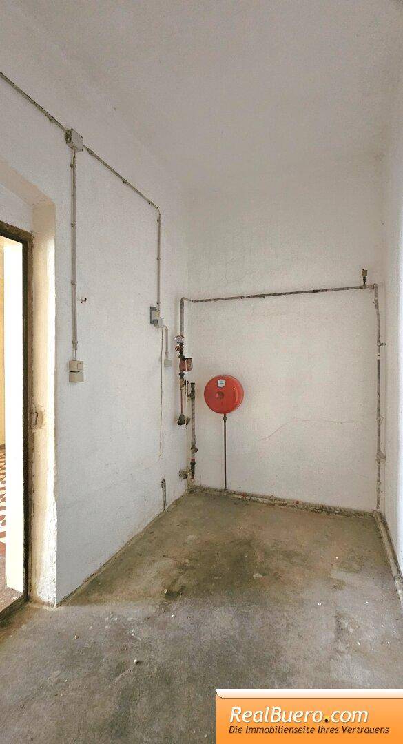 Abstellraum mit sichtbaren Leitungen und einem roten Feuerlöscher an der Wand.
