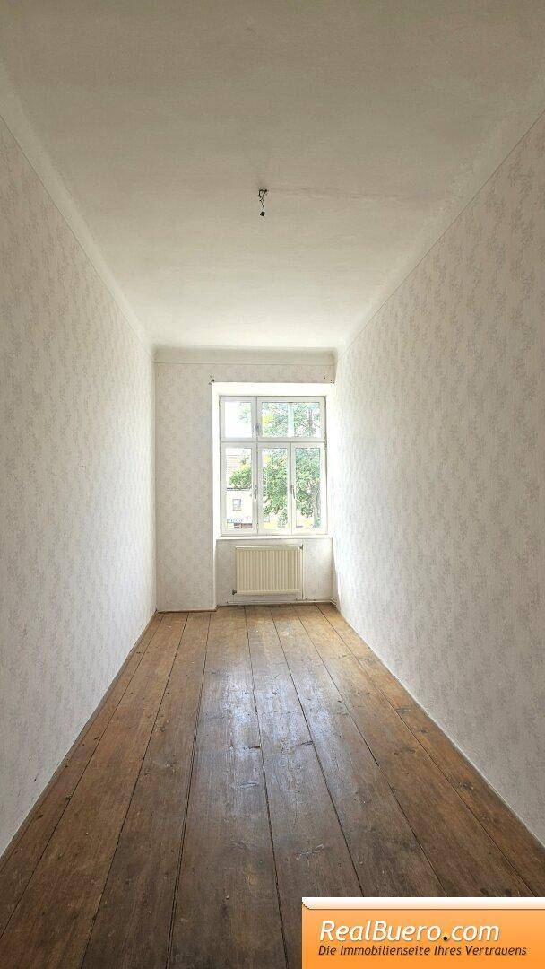 Schmaler Raum mit Holzdielenboden und einem Fenster, ideal als Schlafzimmer oder Arbeitszimmer.