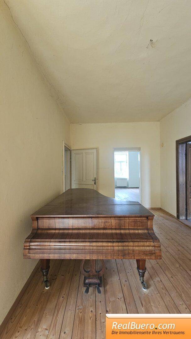 Geräumiges Zimmer mit Holzdielenboden und einem Flügel, ideal als Wohn- oder Musikzimmer.