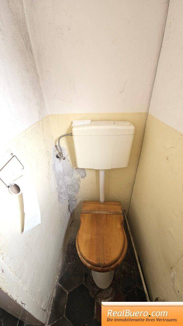 Kleines WC mit traditioneller Toilette und sechseckigem Fliesenboden, in einfachem Zustand.