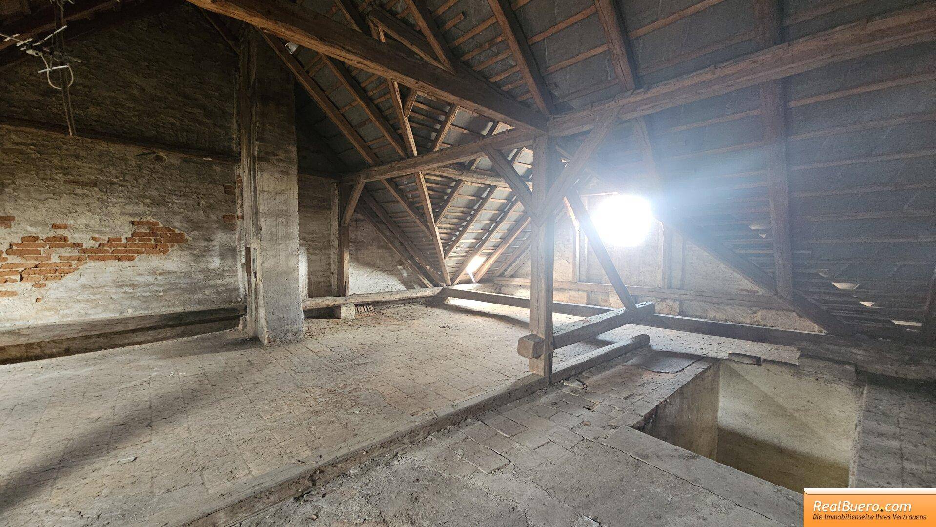 Geräumiger, unfertiger Dachboden mit sichtbarer Holzbalkenkonstruktion und Ziegelwänden, bereit für Ausbau.