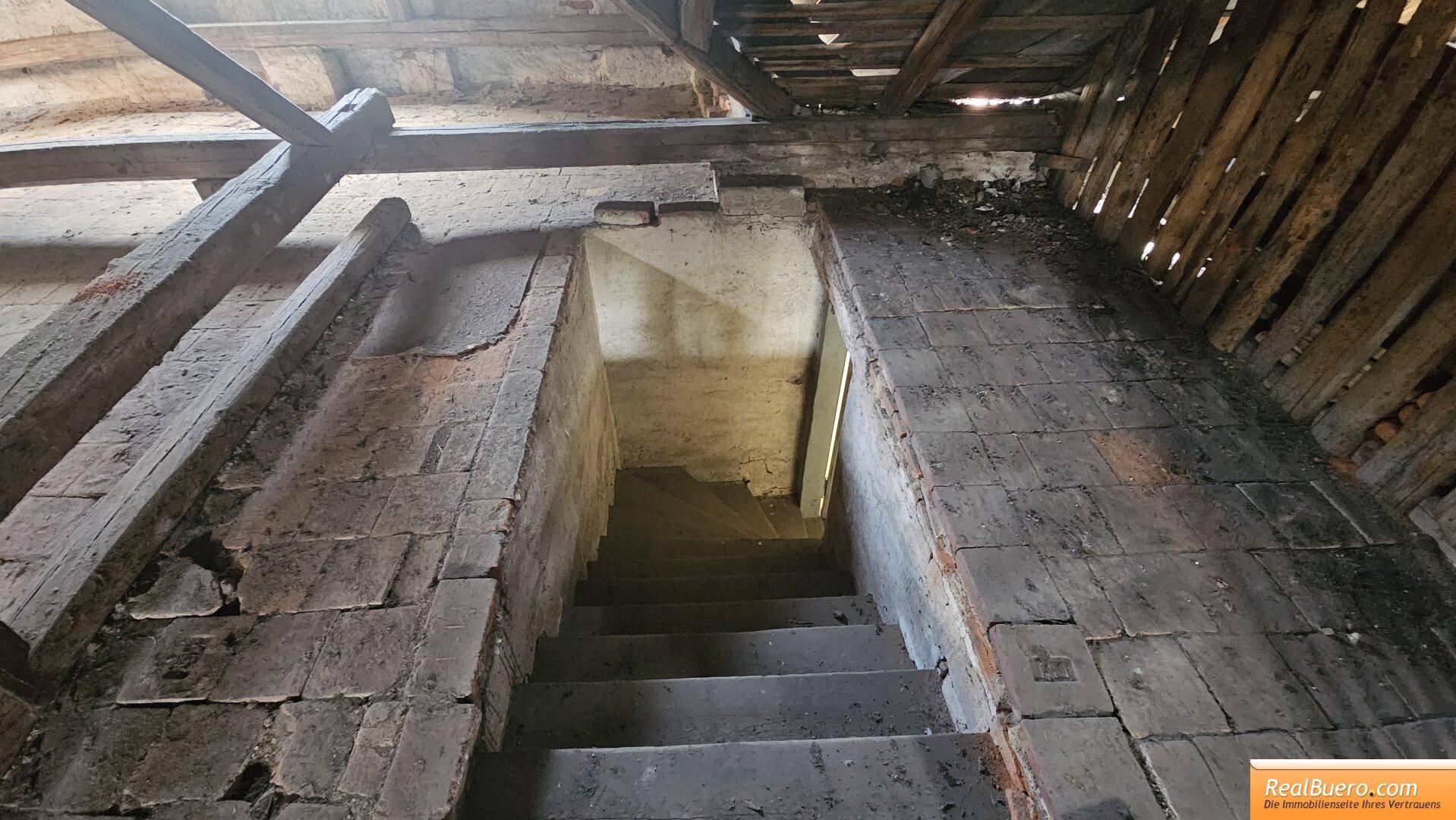 Steile Treppe führt vom Dachboden hinunter, umgeben von unverputzten Ziegelwänden.