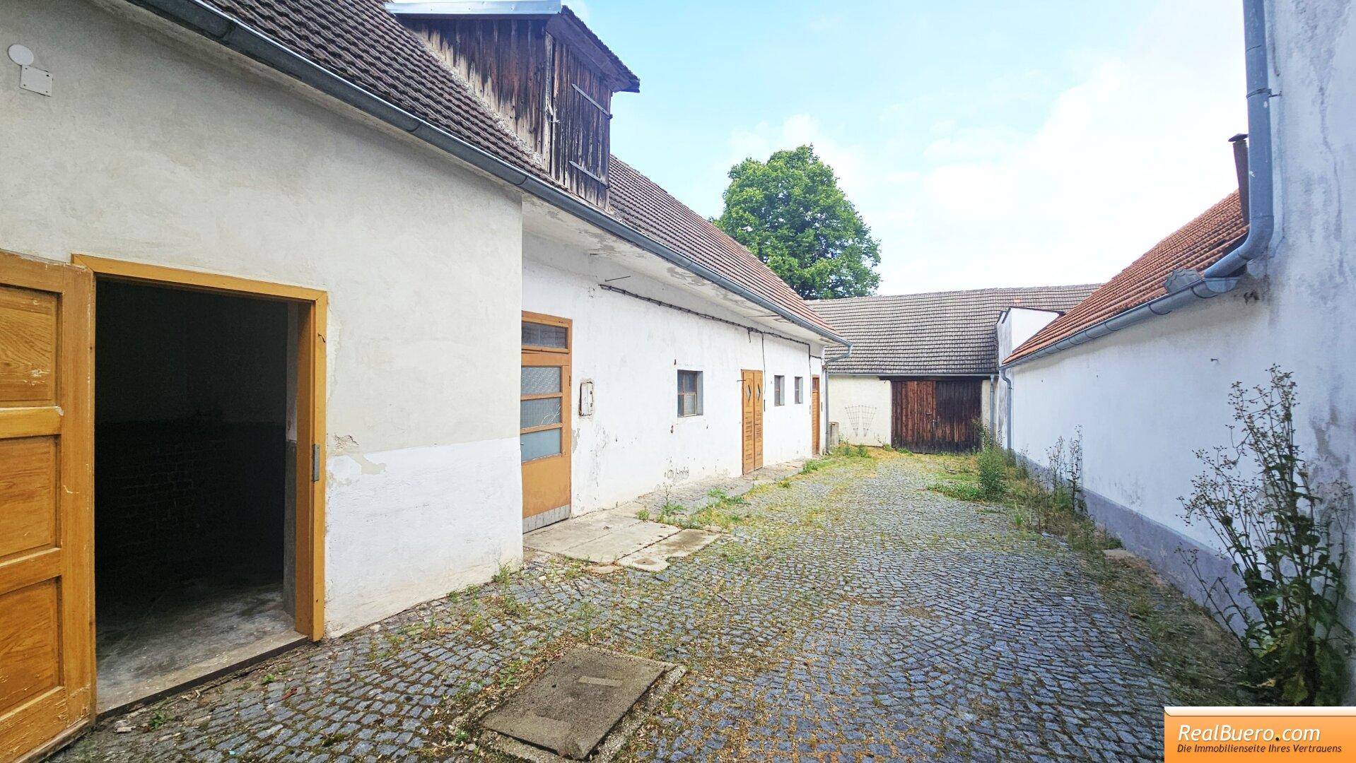 Gepflasterter Innenhof zwischen mehreren Gebäuden mit weißen Fassaden und Holztüren.