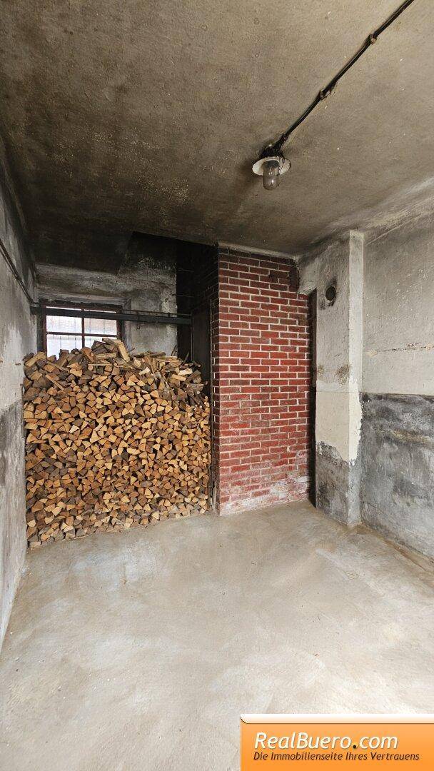 Kellerraum mit Brennholzstapel und einer freistehenden Ziegelwand, bietet viel Stauraum.