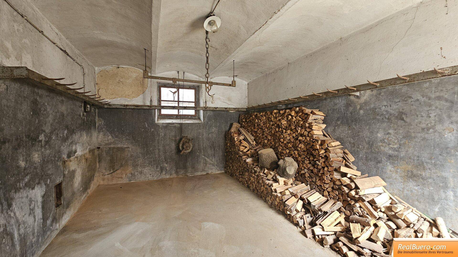 Kellerraum mit gestapeltem Brennholz, einem kleinen Fenster und unverputzten Wänden.