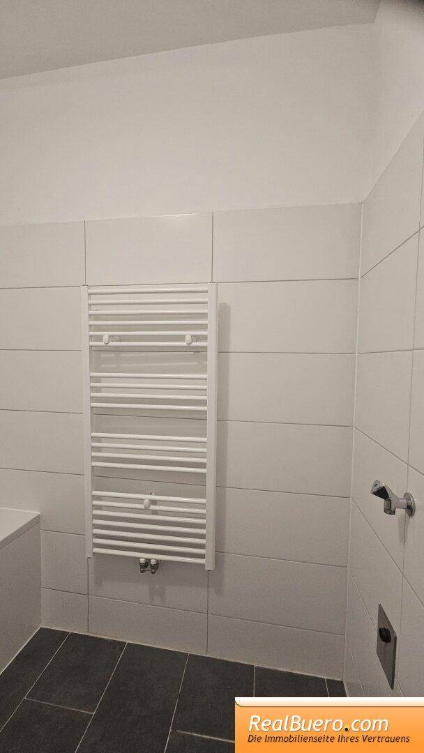 Badezimmerdetail mit modernem beheiztem Handtuchhalter und weißen Wandfliesen.