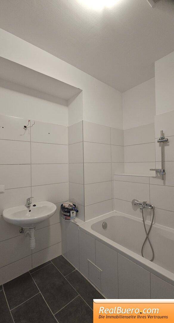 Helles Badezimmer mit Badewanne, Waschbecken und weißen Wandfliesen.