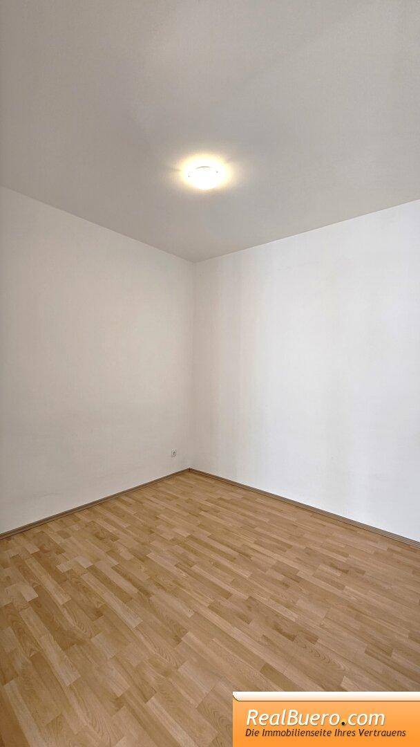 Leerer Raum mit hellem Laminatboden und weißen Wänden, bereit zur individuellen Gestaltung.