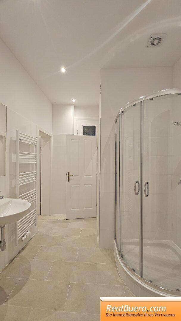 Modernes Badezimmer mit Duschkabine, Waschbecken und hellen Fliesen, in gutem Zustand.
