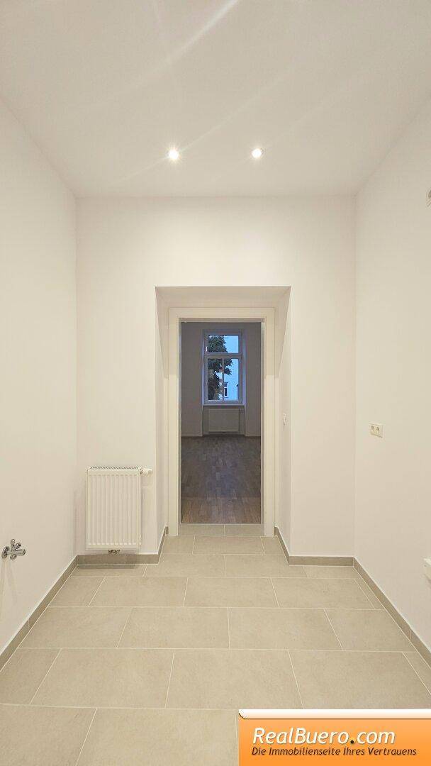 Eingangsbereich mit Fliesenboden und Blick in ein angrenzendes Zimmer mit Parkett.