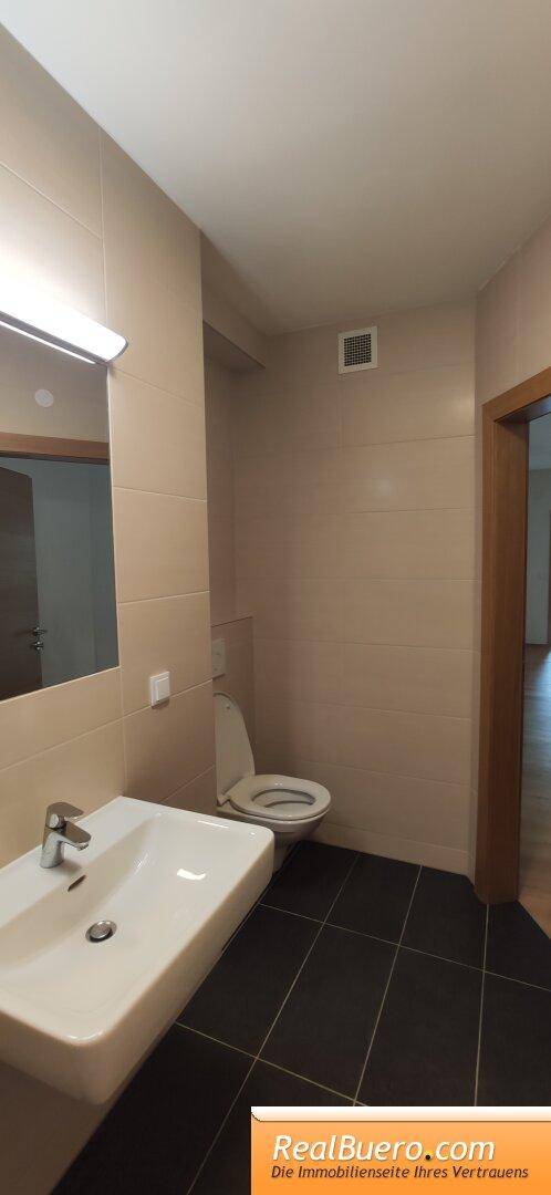 Modernes Badezimmer mit Waschbecken, Toilette und dunklen Bodenfliesen.