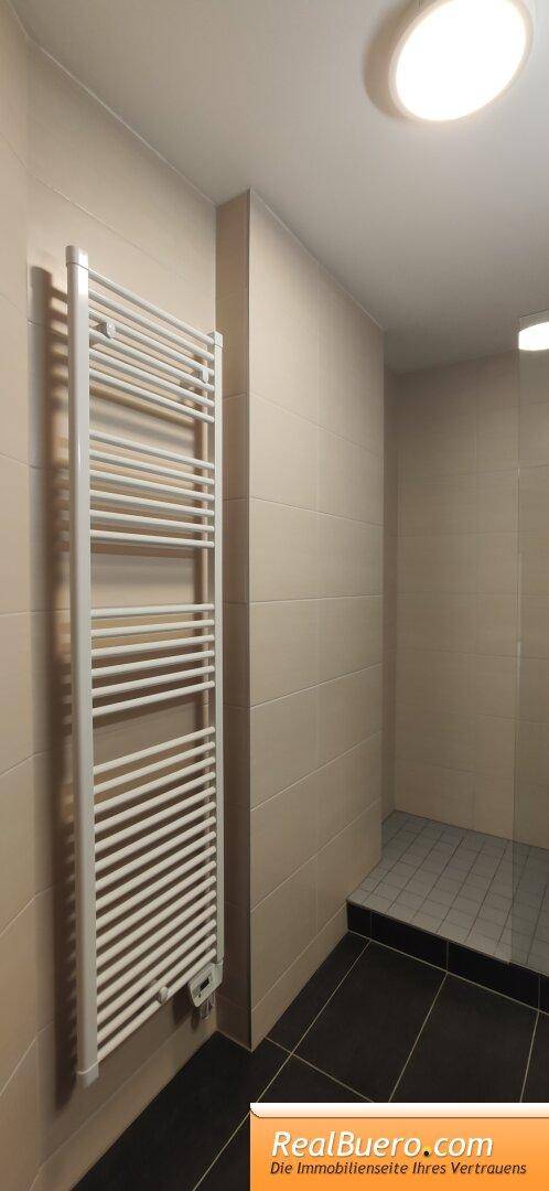 Badezimmer mit beheiztem Handtuchhalter und Duschbereich, hell gefliest.