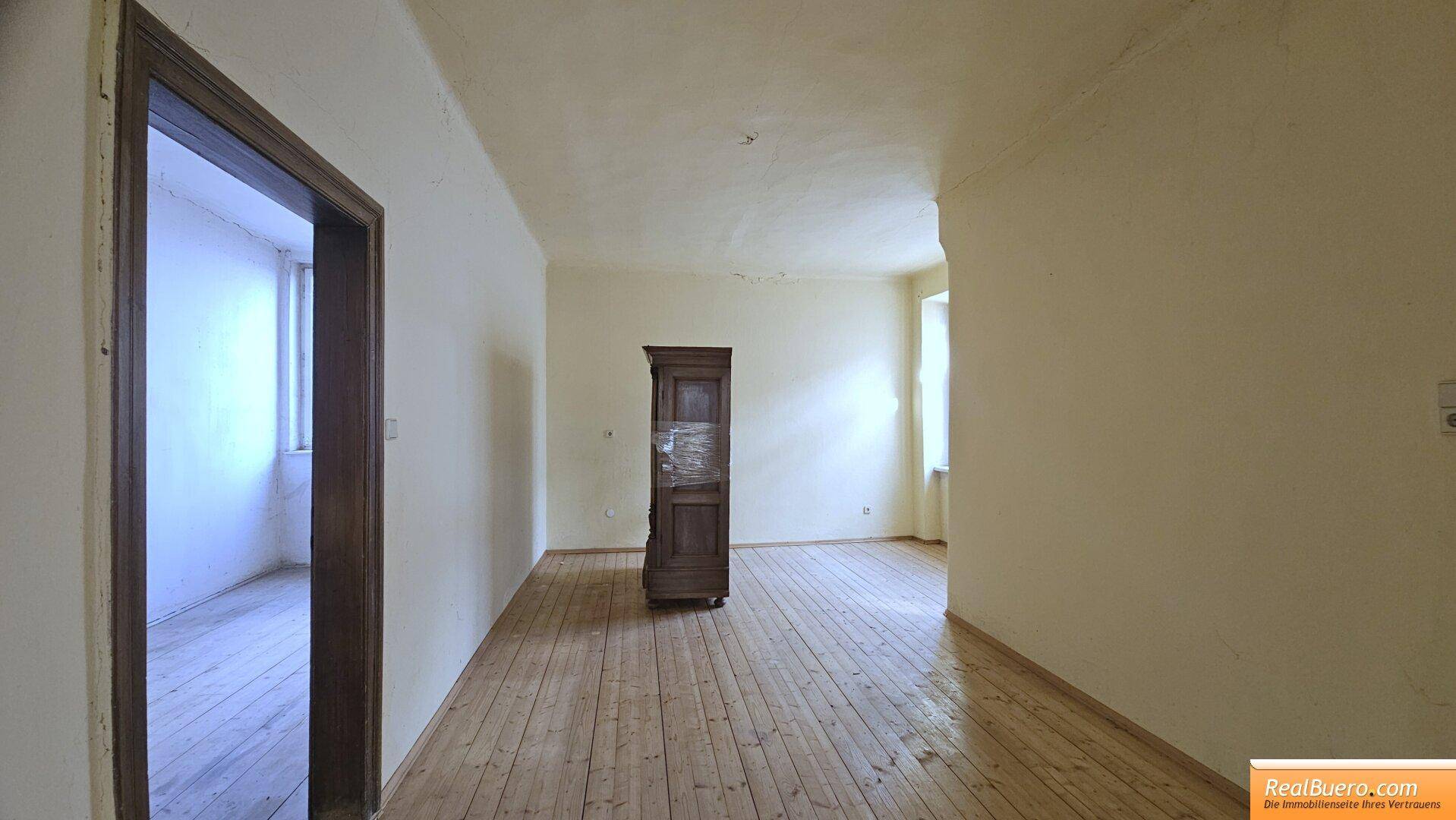 Geräumiges Zimmer mit Holzplankenboden und einem antiken Holzschrank, bereit zur Einrichtung.