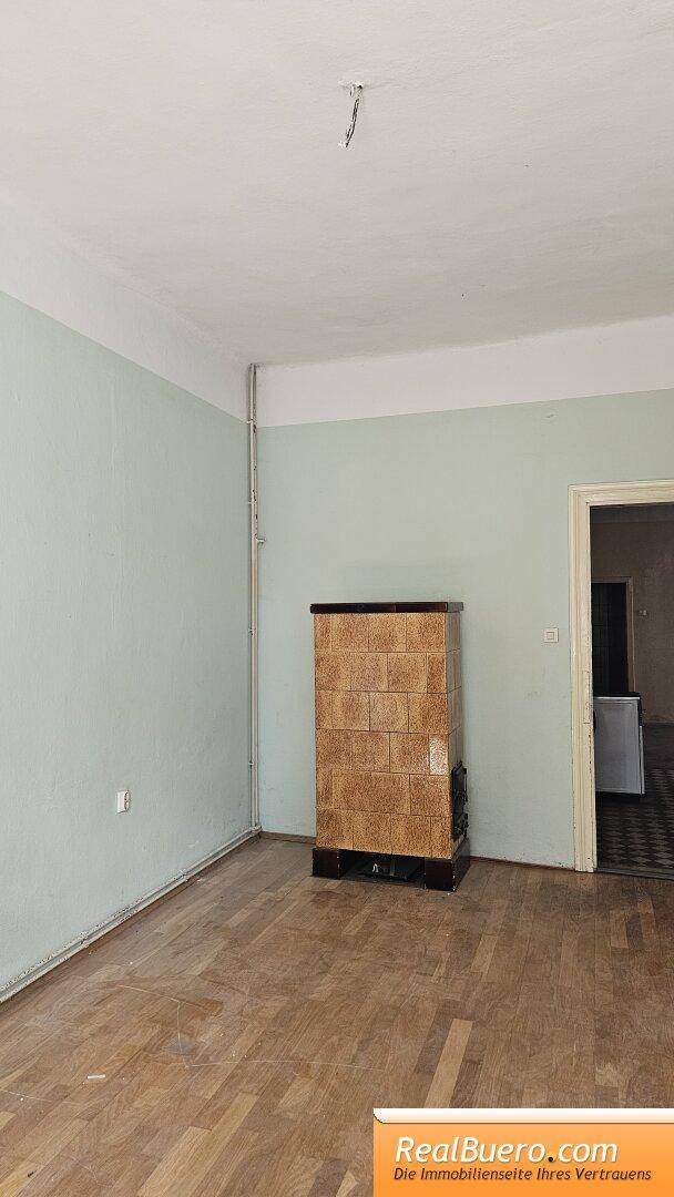 Geräumiges Zimmer mit Holzplankenboden und einem traditionellen Kachelofen als Heizquelle.