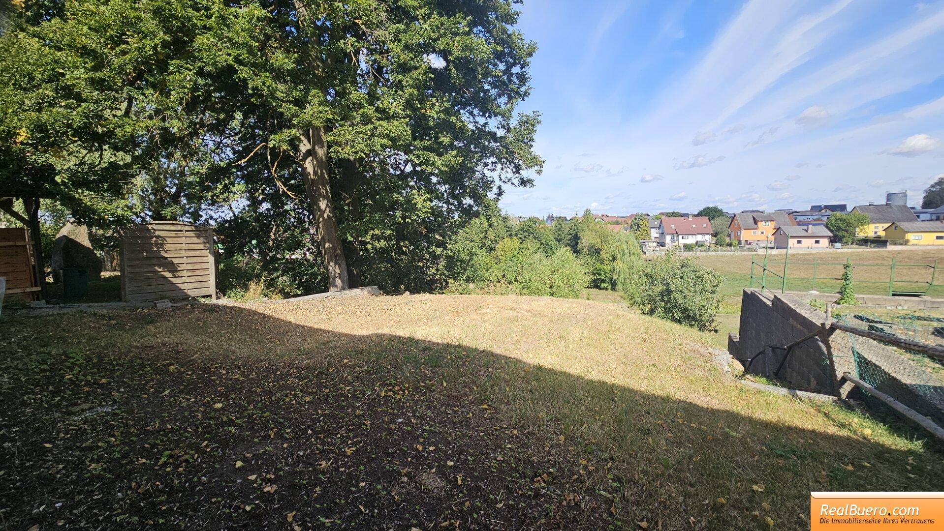 Außenbereich mit trockenem Gras und Bäumen, bietet einen weiten Blick auf die umliegenden Häuser.