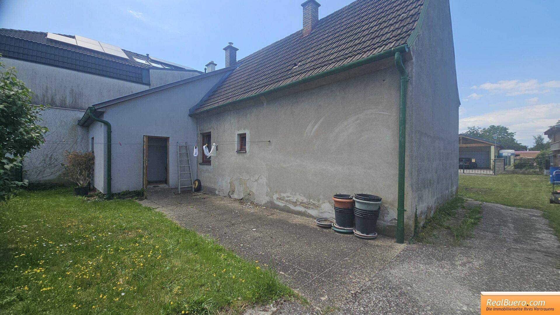 Seitenansicht des Hauses mit einem Betonweg, einer Tür und einigen Pflanzgefäßen im Gartenbereich.