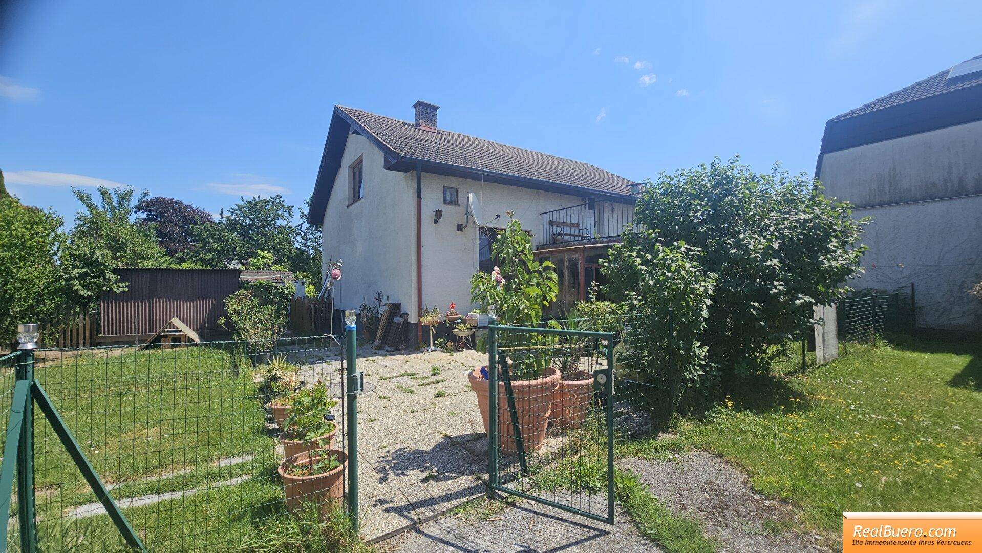 Rückansicht des Hauses mit gepflastertem Bereich, Topfpflanzen und einem kleinen Balkon über dem Garten.