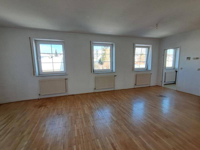 Heller Wohnbereich mit mehreren Fenstern und Holzparkettboden, ideal für individuelle Gestaltung.