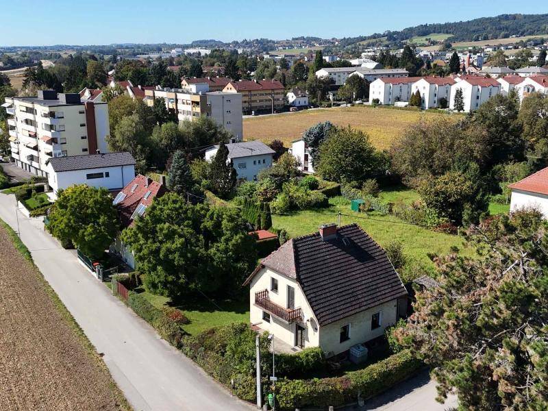 Übersichtsaufnahme des Hauses mit Garten, umgeben von Wohngebäuden und Feldern in der Ferne.
