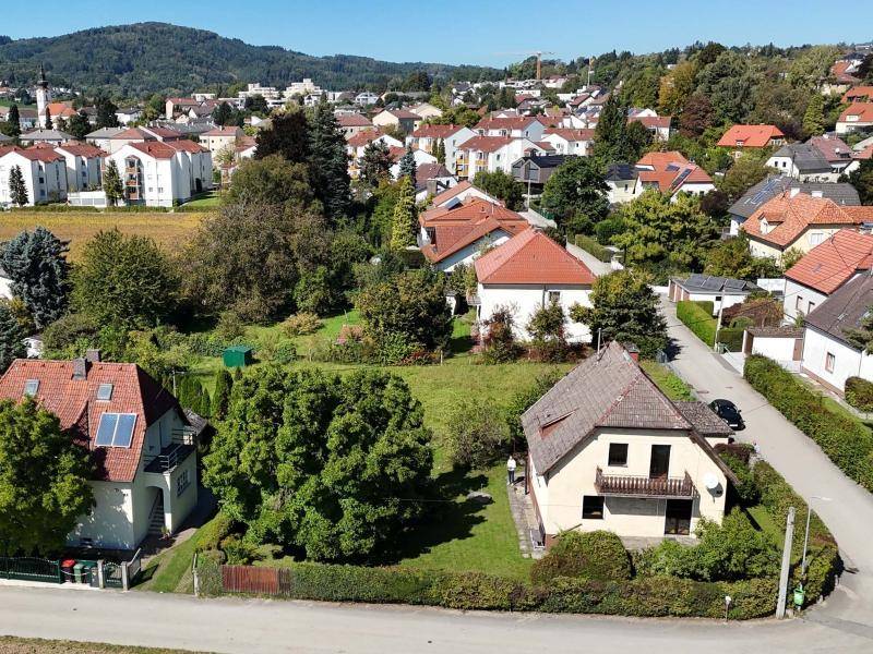 Weitläufige Luftaufnahme des Hauses mit Garten, umgeben von einer Wohnsiedlung und grünen Hügeln.