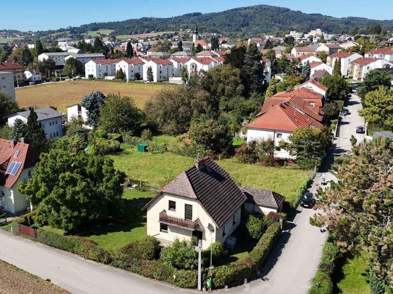 Weitläufige Luftaufnahme des Hauses mit Garten, umgeben von einer Wohnsiedlung und grünen Hügeln.