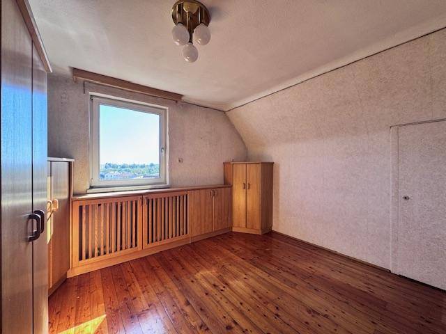 Schlafzimmer mit Holzboden, Einbauschränken und einem Fenster unter der Dachschräge.